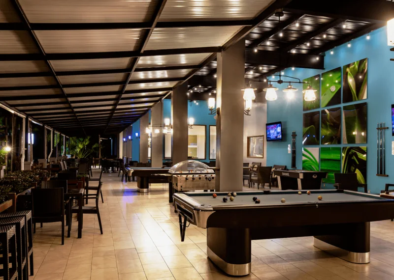The Livingroom games terrace at night: pool tables, foosball, café tables under a covered walkway, backlit