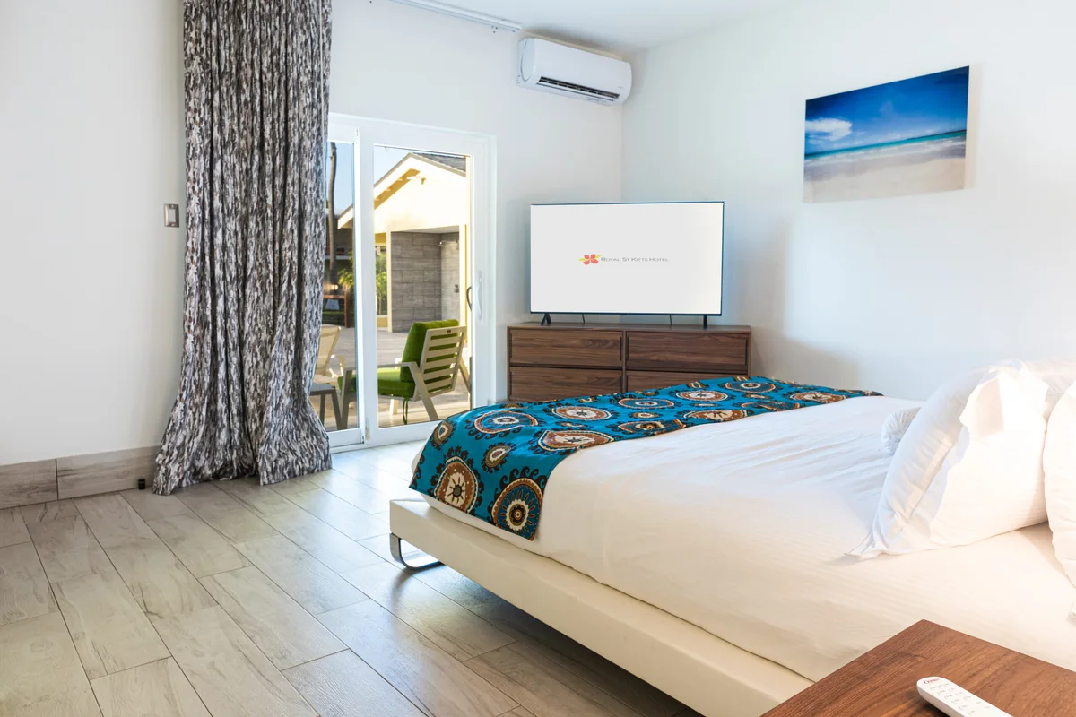 Bedroom with platform bed, teal-and-brown patterned runner, walnut dresser, sliding door onto a patio; TV shows