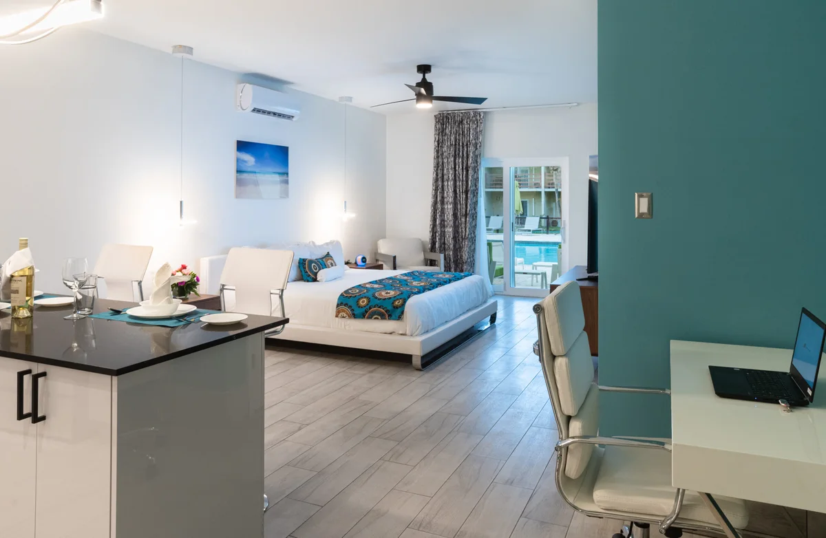 Studio/junior suite: kitchen bar counter foreground, king bed centre, desk and office chair right, sliding door