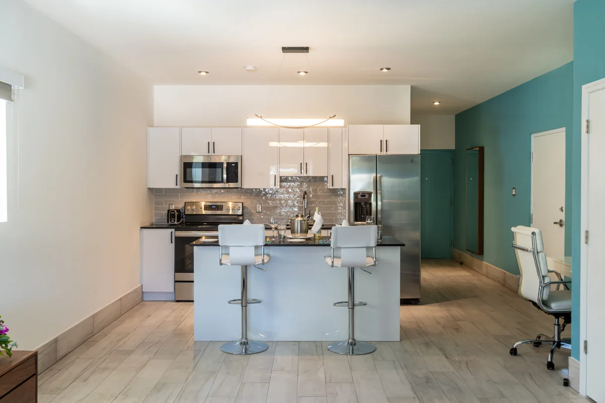 White gloss kitchen with grey subway backsplash, stainless range/microwave/fridge, island with two white