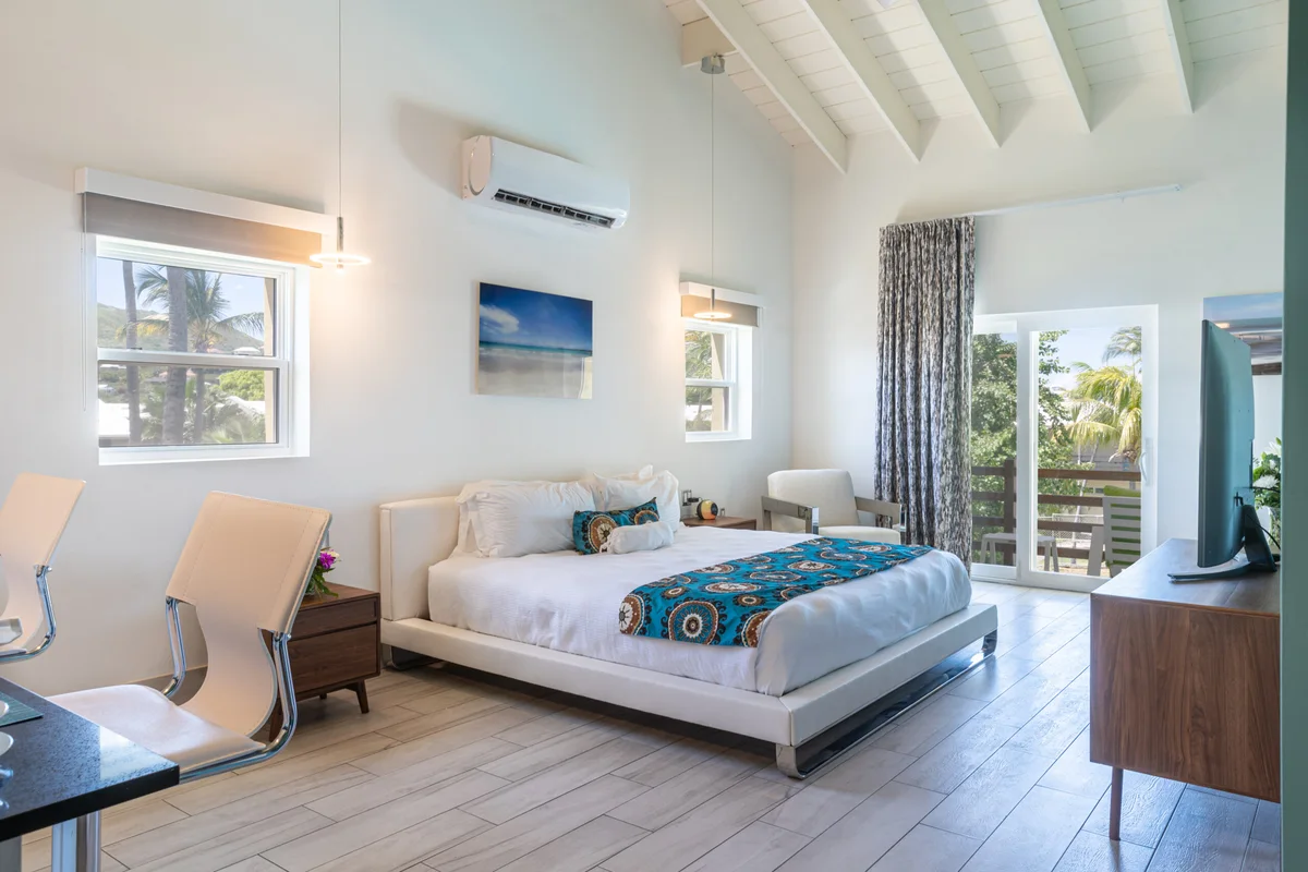 Bedroom with vaulted white beamed ceiling, king platform bed, two sash windows, balcony door onto a timber deck