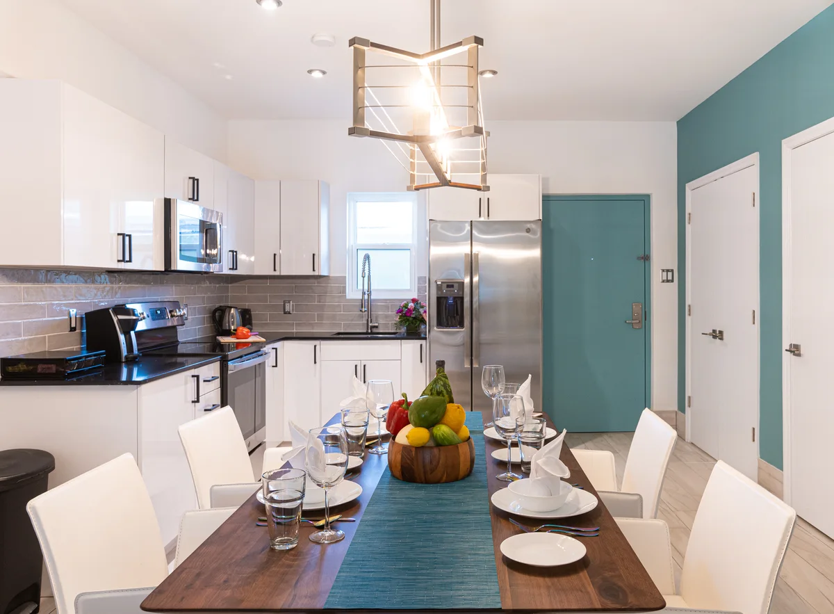 Open kitchen and dining area: white gloss kitchen with grey tile, walnut table set for six, turquoise unit