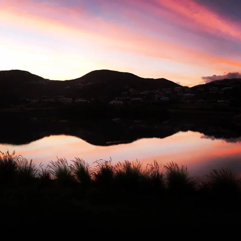 Pink-and-orange sunset over the lake beside the property, hillside houses silhouetted and mirrored in still