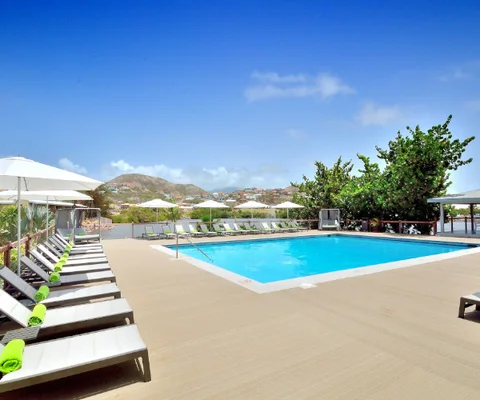 Pool terrace with white umbrellas and green-towelled loungers, open view to the Frigate Bay hillside