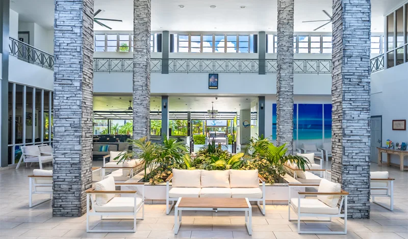 Double-height lobby atrium: stacked-stone columns, white lounge seating, central planter, sea artwork on the