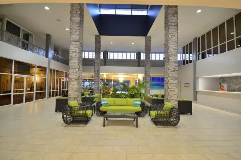 Lobby with lime-green sofa and woven tub chairs between stone columns, front desk with a staff member at right