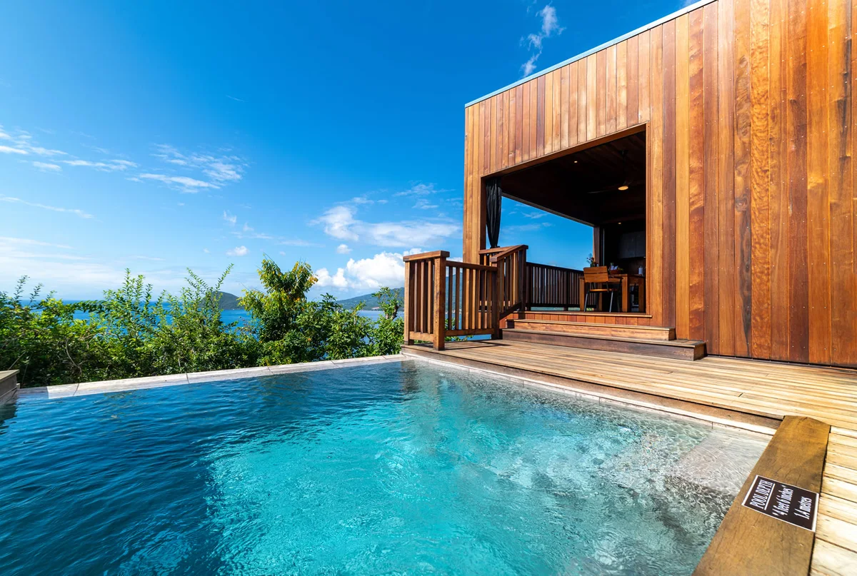 PHOTO — close view of the plunge pool beside the timber villa wall, sea and sky beyond. 1600x1076
