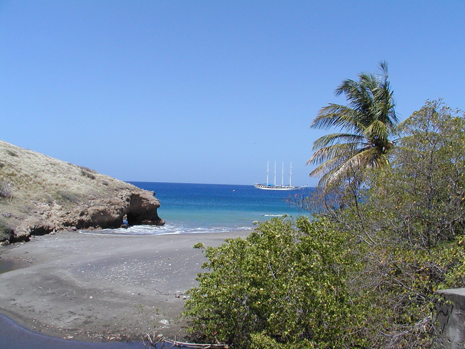 A grey-sand cove with a tall ship anchored offshore, Montserrat